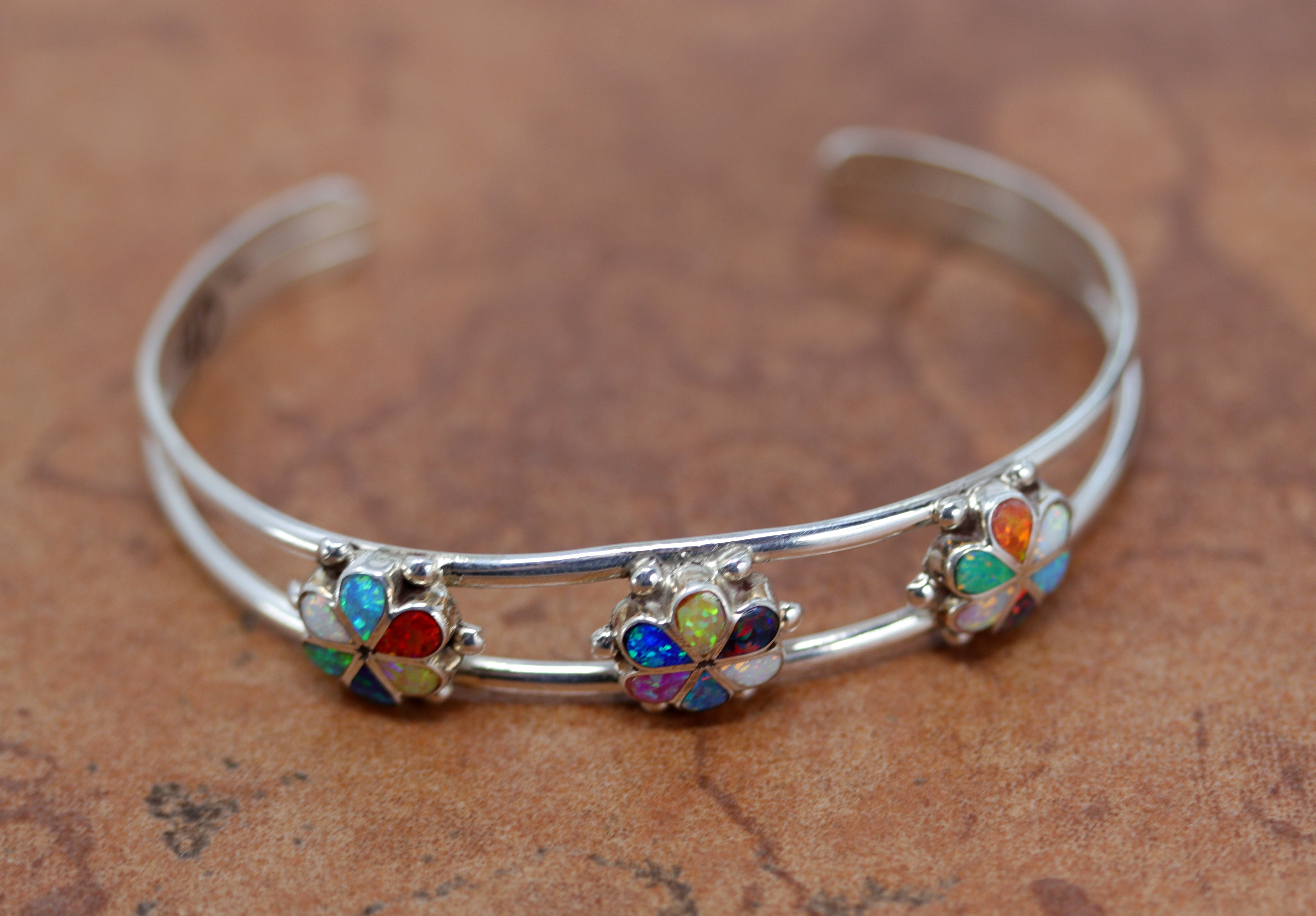 Silver cuff bracelet with three multi colored flower stones. It includes white, orange, blue, and white colored opal stones