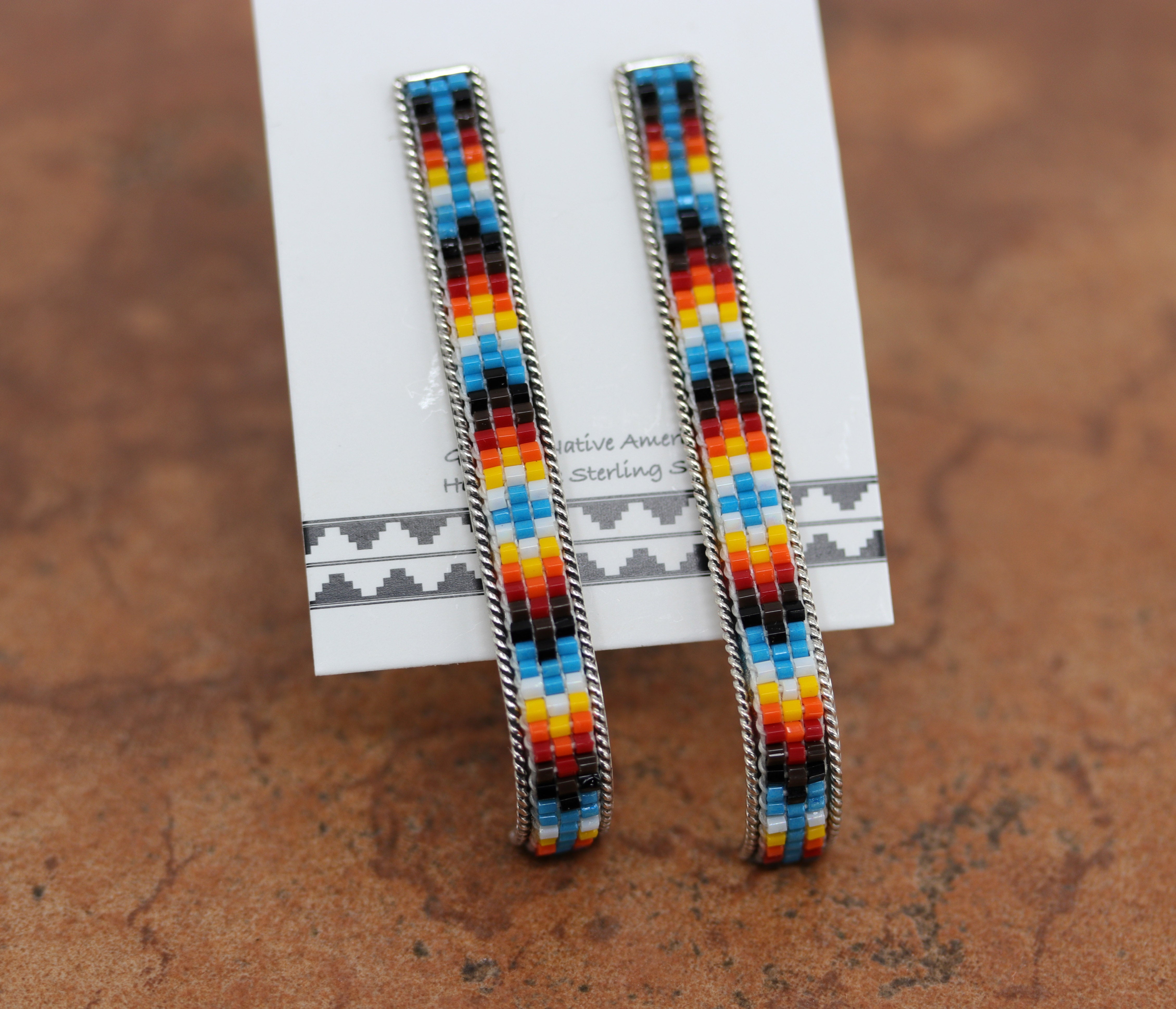 Long rectangular post earrings with beads that are blue, yellow, red, orange, black, and white