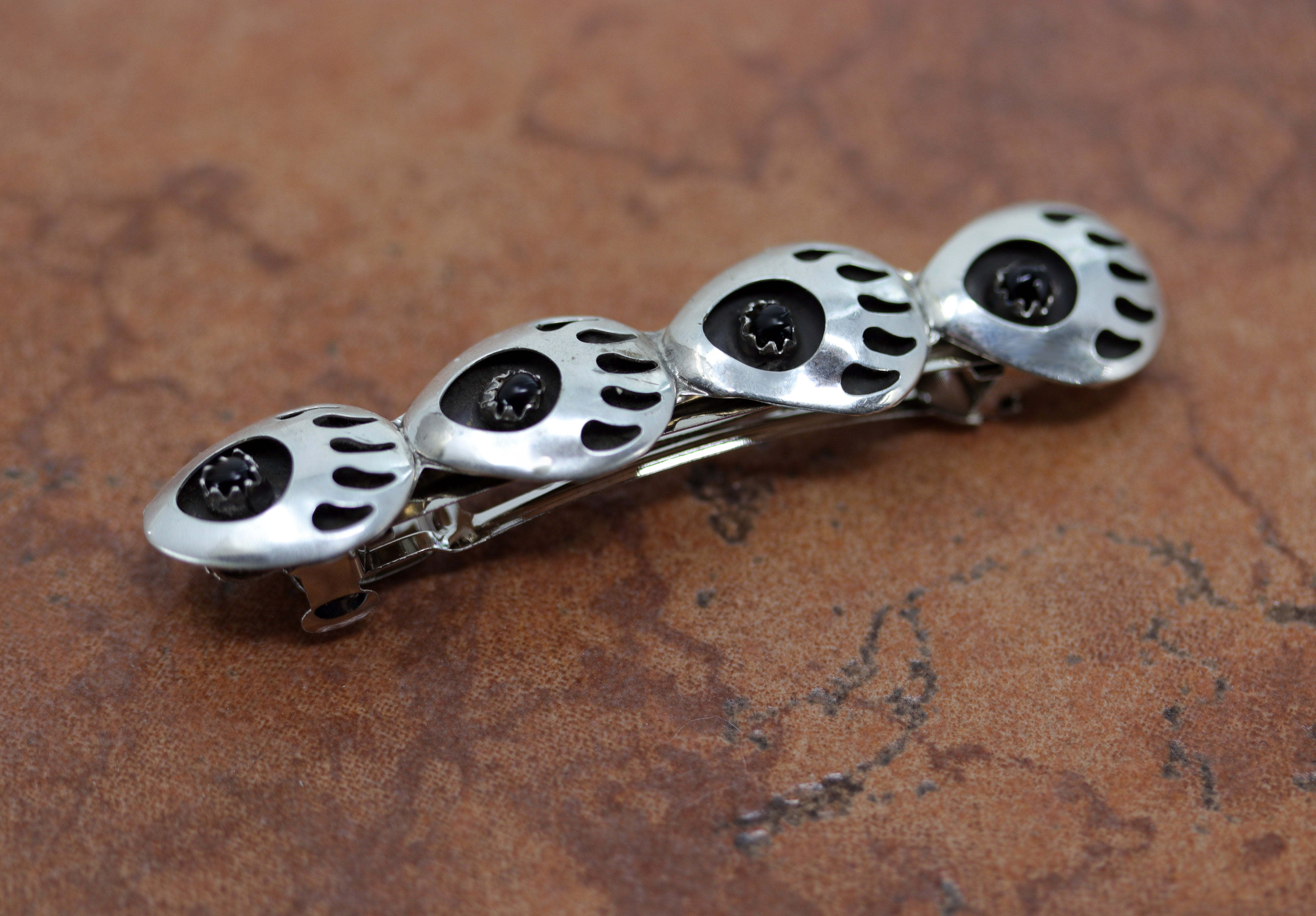 Silver barrette that contains 4 bear paws each with a small black onyx stone inside of it