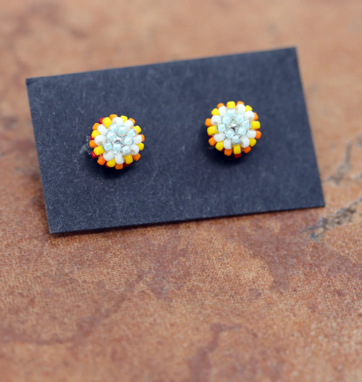 Circular post earrings made from multi colored beads that are mostly white with yellow and orange beads as well