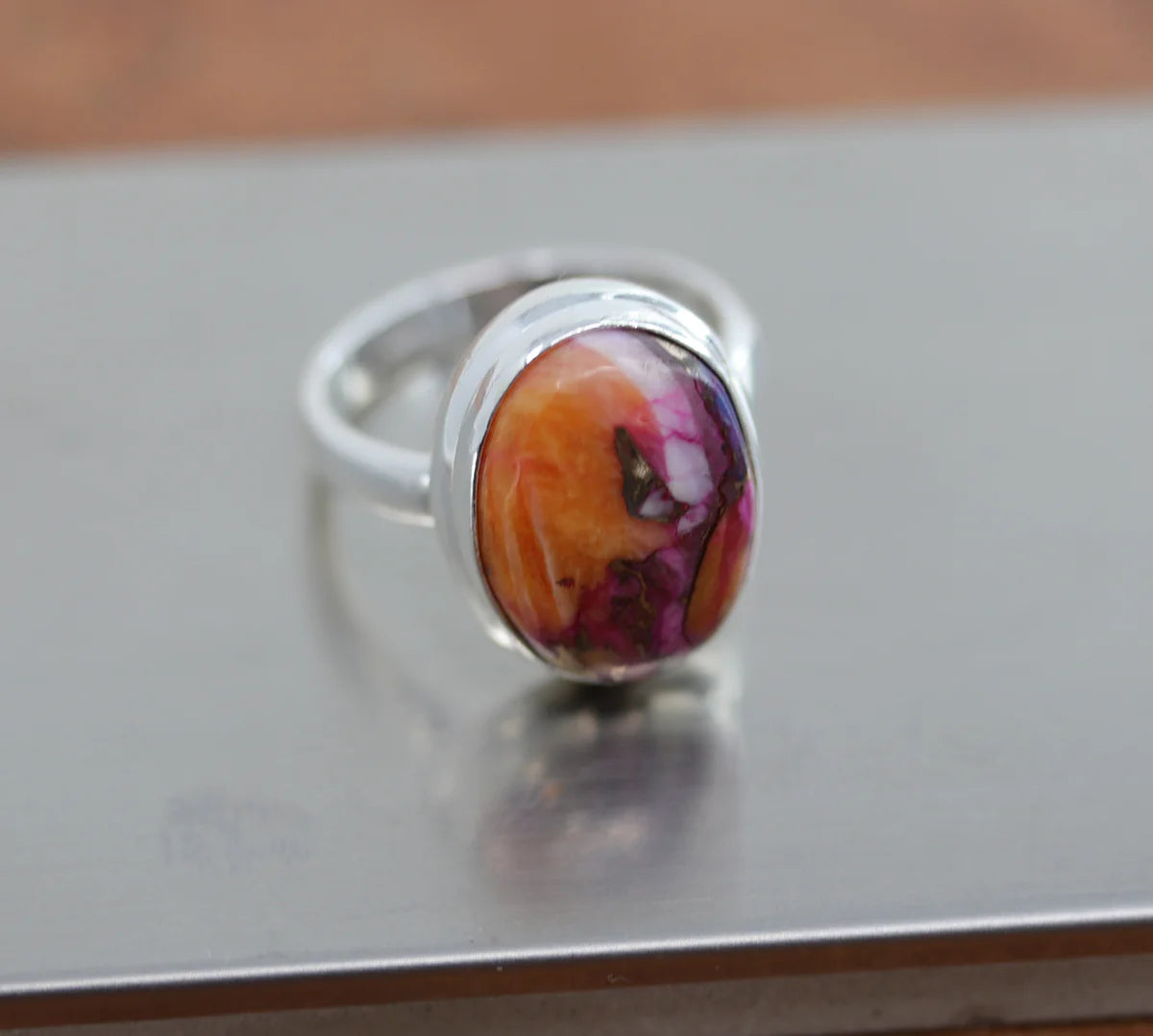 Silver ring with a circular gemstone that's mostly orange with bits of turquoise